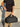 Person holding a black duffel bag against a stone wall.